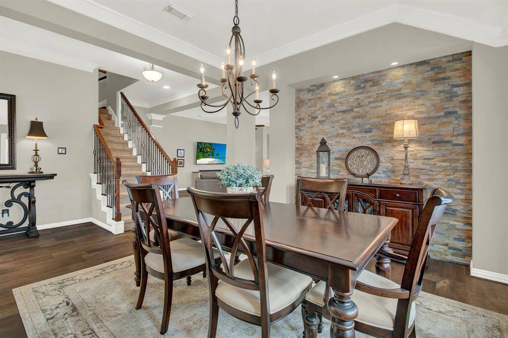 This dining area features elegant wood flooring, a stylish chandelier, and a rustic stone accent wall. The room offers ample space with a classic dining set, and the open layout leads to a staircase, enhancing the home's charm and flow.
