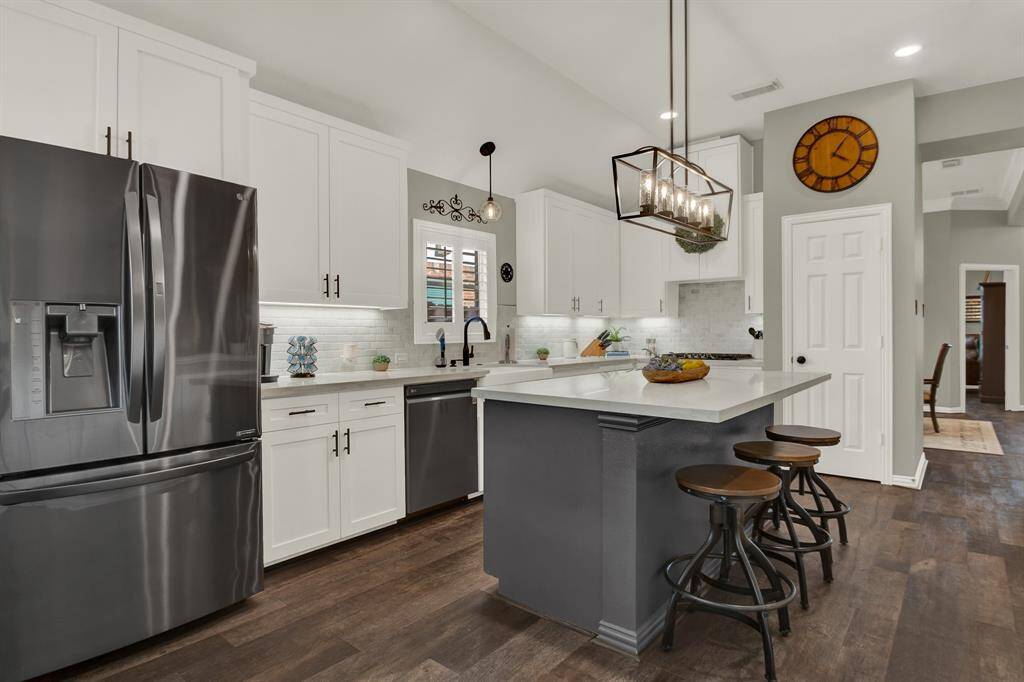 The kitchen features modern stainless steel appliances, white cabinetry, and a central island with seating.