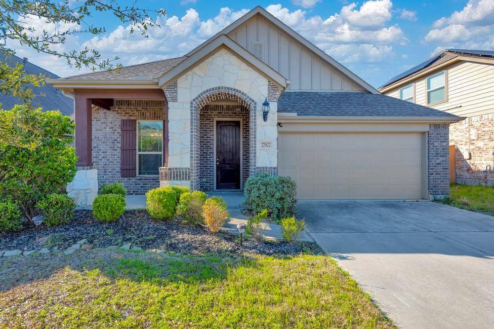 Charming single-story home with a welcoming front porch, brick façade, and a spacious two-car garage. The well-maintained lawn and cozy exterior lighting create inviting curb appeal, set against a beautiful sunset backdrop.