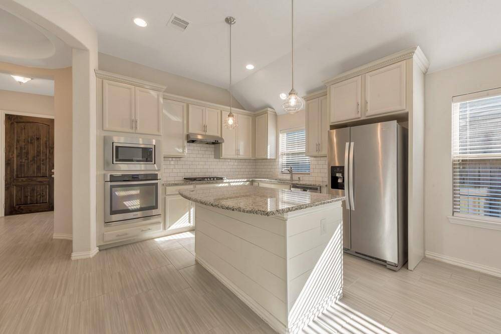 This kitchen features modern stainless steel appliances, light cabinetry, and a spacious granite island. It has a bright, open feel with large windows and pendant lighting, perfect for cooking and entertaining.