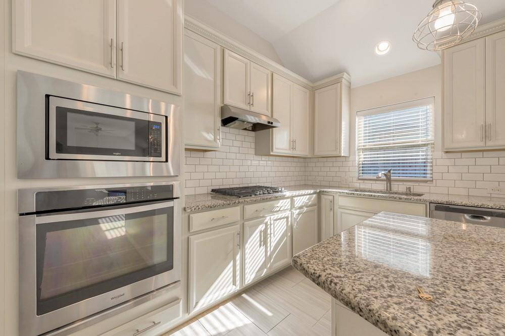 This kitchen features modern stainless steel appliances, white cabinetry, and granite countertops. It has a subway tile backsplash, ample natural light, and a spacious layout ideal for cooking and entertaining.