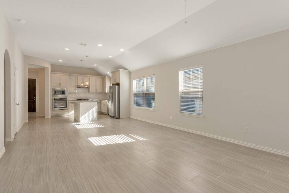 This photo showcases a spacious, open-plan kitchen and living area with modern finishes. The kitchen features stainless steel appliances, an island, and ample cabinetry. Large windows provide natural light, highlighting the neutral-toned flooring and walls. Ideal for entertaining and family living.