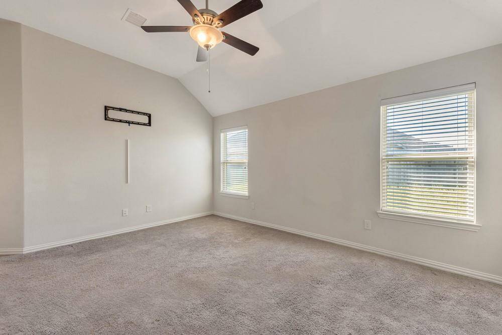 This room features neutral walls, plush carpeting, and a ceiling fan with light. Two windows provide natural light, creating a bright and inviting space.