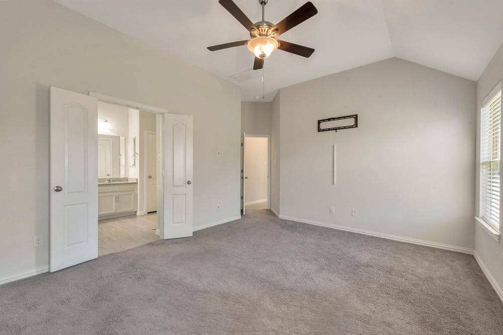 Spacious bedroom with neutral walls and carpet, featuring a ceiling fan and ample natural light. French doors open to an ensuite bathroom with a dual vanity.
