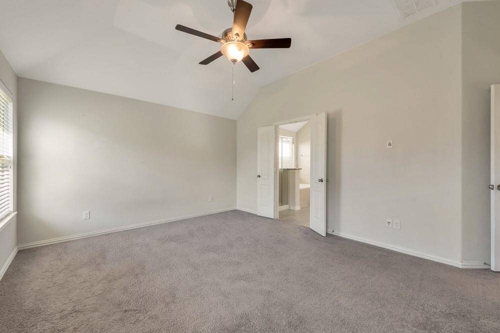 Spacious bedroom with neutral walls, carpeted floor, and a ceiling fan. It features ample natural light from a window and has double doors leading to an adjoining bathroom.
