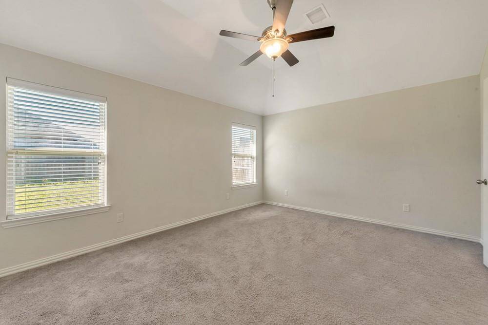 This is a bright, spacious bedroom featuring neutral walls, soft carpet, two windows with blinds, and a ceiling fan with light. Perfect for creating a cozy personal retreat.