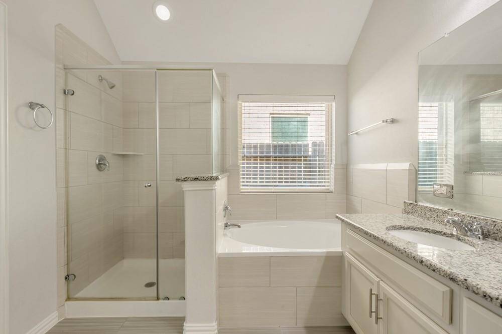 This bathroom features a sleek design with a glass-enclosed shower, a spacious bathtub, and a large vanity with granite countertops. Neutral tiles and a window provide a bright, modern feel.