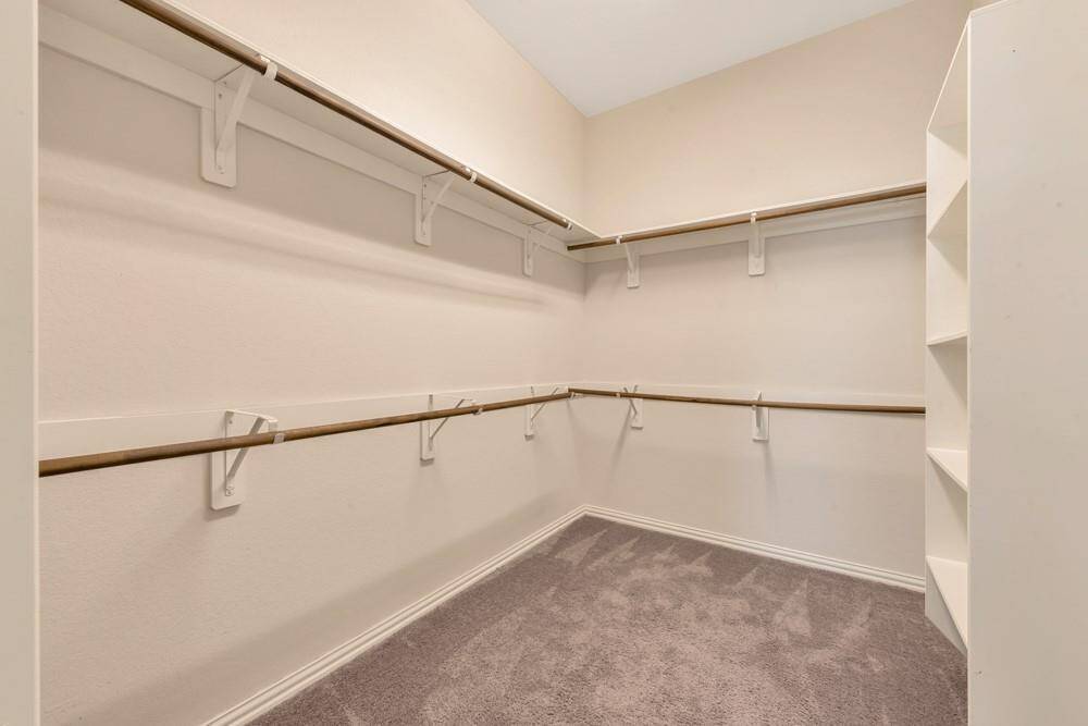 This photo shows a spacious walk-in closet with multiple hanging rods and built-in shelving, offering ample storage space. The neutral color scheme and carpeted floor add a touch of warmth and coziness.