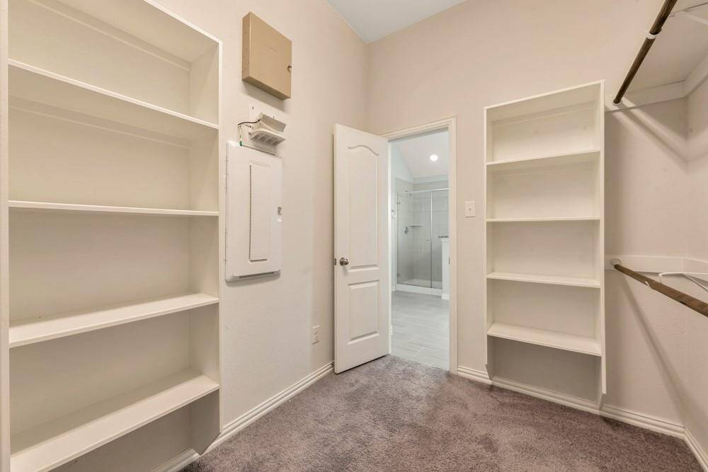 This photo showcases a spacious walk-in closet with built-in shelves and hanging rods. The area is carpeted and leads into a bathroom with a tiled floor, visible through an open door. The neutral color scheme enhances the bright and clean appearance.