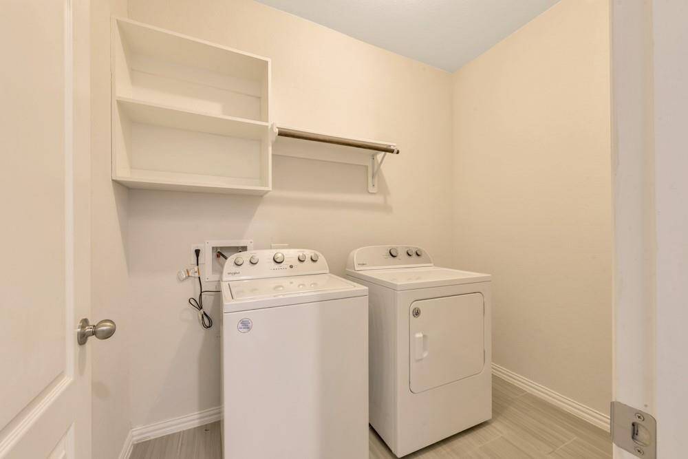 This photo shows a well-lit laundry room featuring a washer and dryer set, with wall-mounted shelves and a hanging rod for additional storage and convenience.