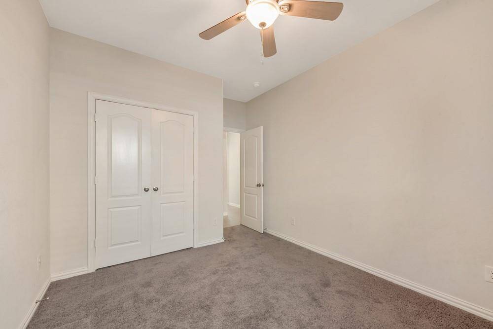 This room features neutral walls, a plush carpet, and a ceiling fan with light. It has a double-door closet and an open doorway leading to another area, making it ideal for a bedroom or home office.
