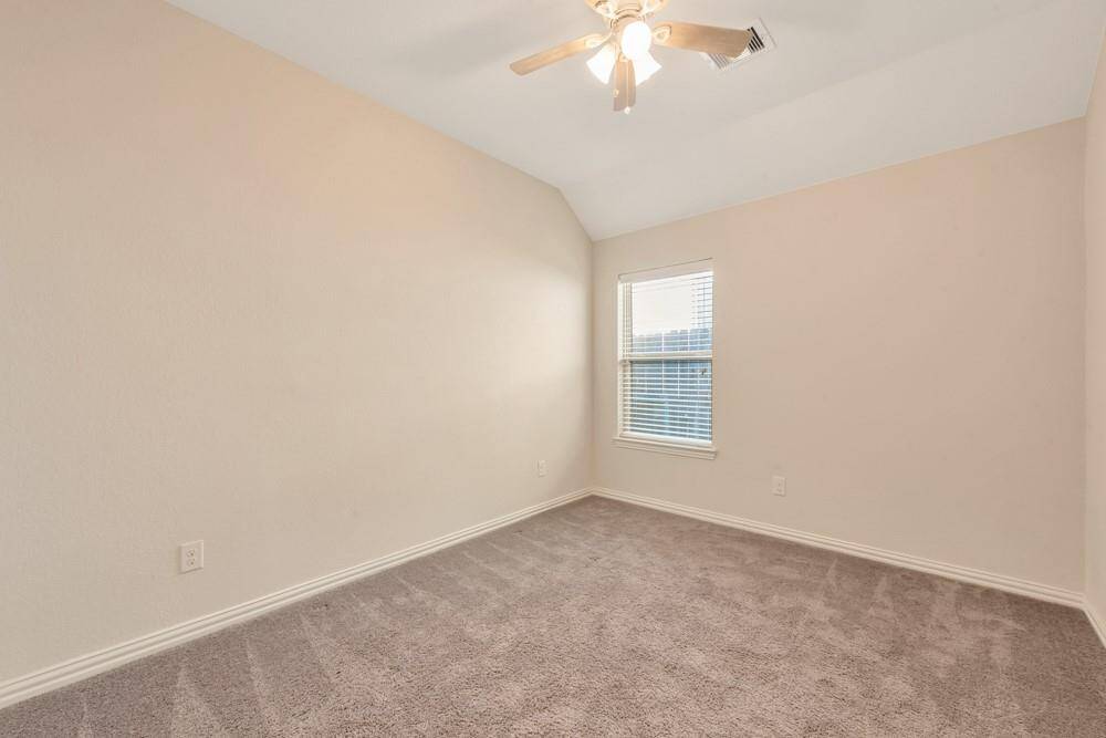 This bright room features neutral walls, plush carpet, a ceiling fan, and a window with blinds, offering a cozy and versatile space.