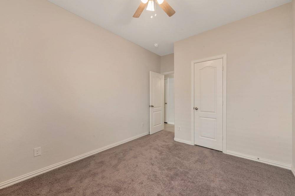 This is a cozy room with neutral walls, carpeted flooring, and a ceiling fan with light. It features a door leading to a hallway and a closet door, creating a functional space suitable for a bedroom or office.