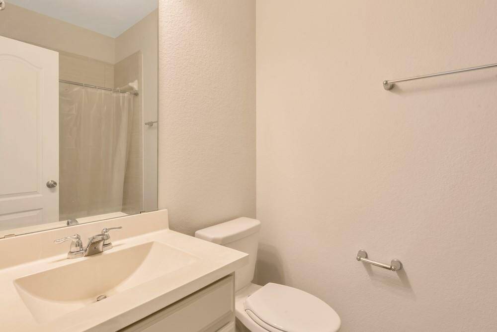 This is a simple, clean bathroom featuring a single sink vanity, a wall mirror, a toilet, and a shower with a curtain. The neutral color scheme provides a bright and open feel.