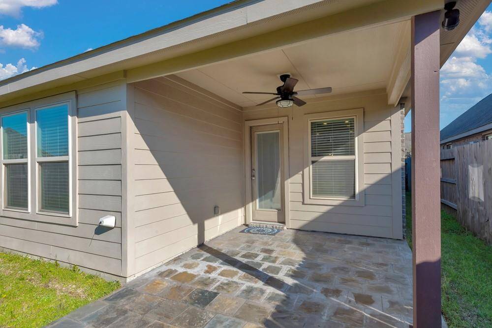 Charming covered patio with a ceiling fan, stone flooring, and ample natural light. Ideal for relaxing or entertaining, with privacy from a wooden fence.