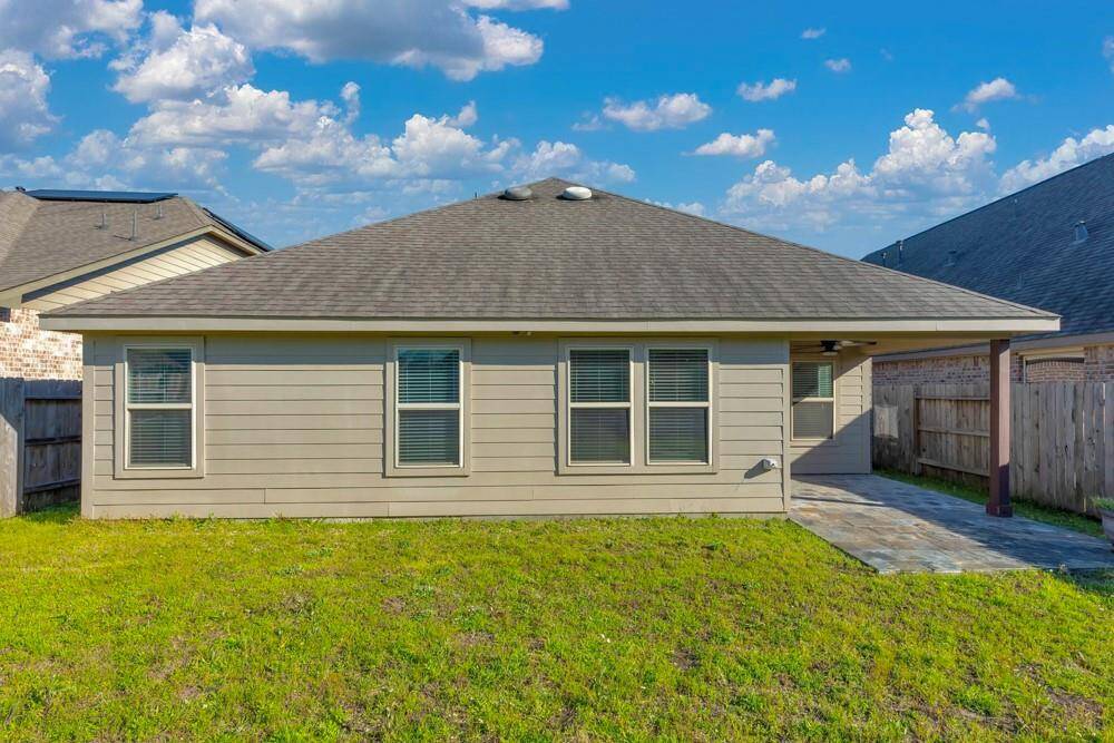 This photo shows the backyard of a single-story home with a neatly maintained lawn and a covered patio area. The house has a simple design with beige siding and several windows. The yard is enclosed by wooden fencing, offering privacy.