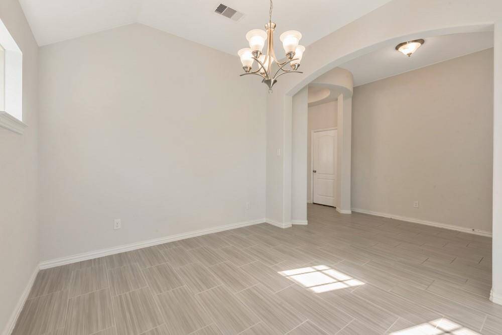 This bright room features light tile flooring, neutral walls, and a stylish chandelier. An arched doorway leads to another space, adding architectural interest and a sense of openness.