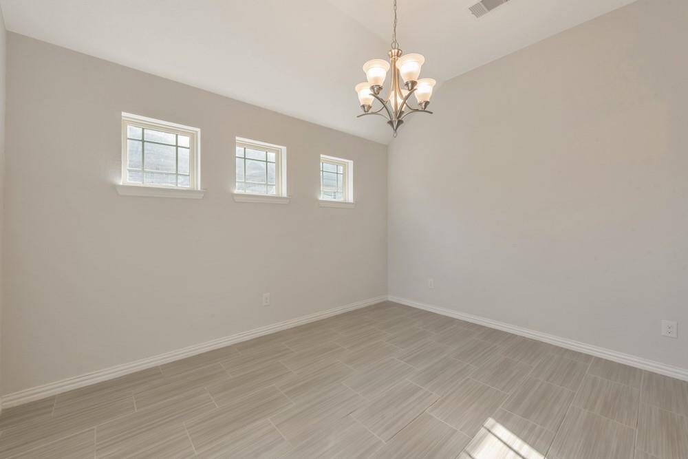 This room features light-colored tile flooring, three small windows for natural light, and a stylish chandelier. The neutral walls enhance the bright and airy feel, making it a versatile space suitable for dining or as an office.