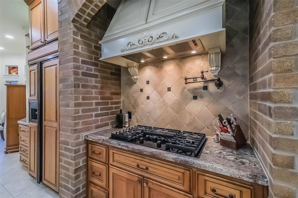 Close up of the gas cooktop with pot filler and decorative vent hood.