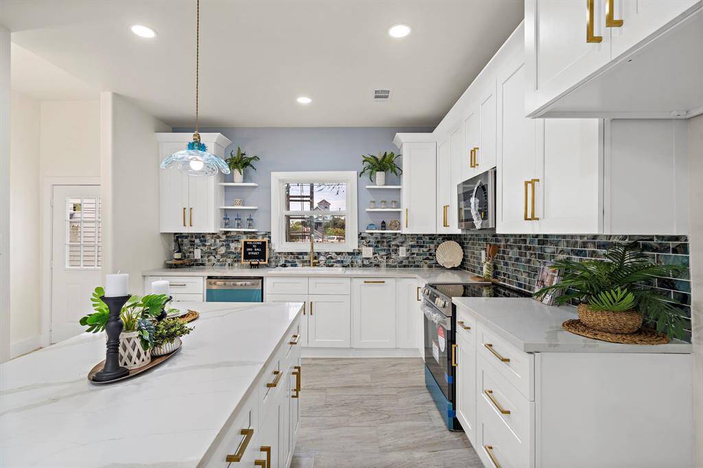 This is a modern and stylish kitchen featuring white cabinetry with gold hardware, elegant quartz countertops, and a unique mosaic tile backsplash. It is well-lit, with recessed lighting and a chic pendant light over the island.