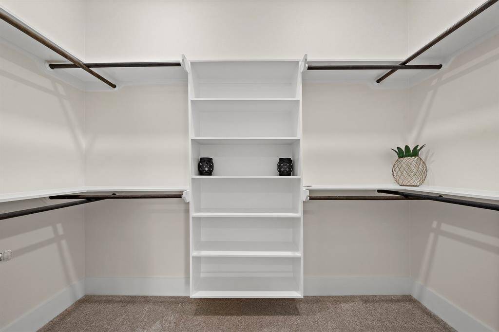 This is a spacious walk-in closet with built-in white shelving and multiple hanging rods, providing ample storage options for clothing and accessories.
