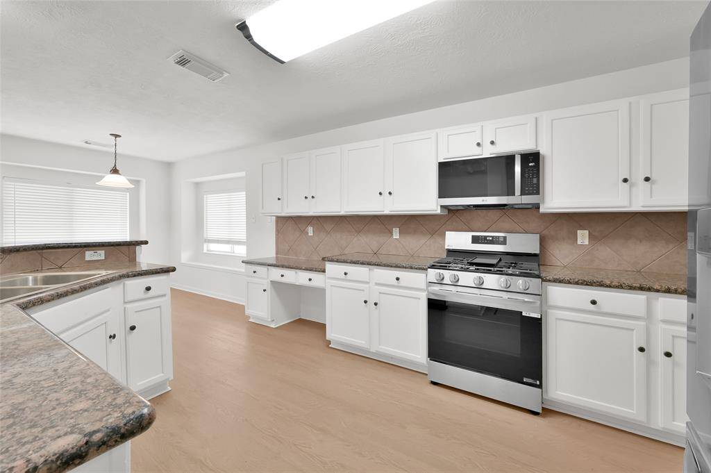 This kitchen features modern stainless steel appliances, white cabinetry, and granite countertops. It has a spacious layout with a breakfast bar, ample natural light, and light wood flooring, creating a bright and welcoming space.