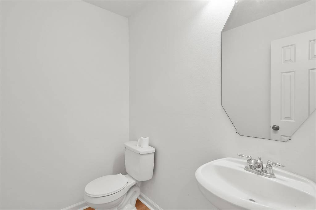 This is a small, minimalist bathroom featuring a toilet, a sink with a modern faucet, and an angular mirror. The walls are painted a light color, enhancing the room's brightness.