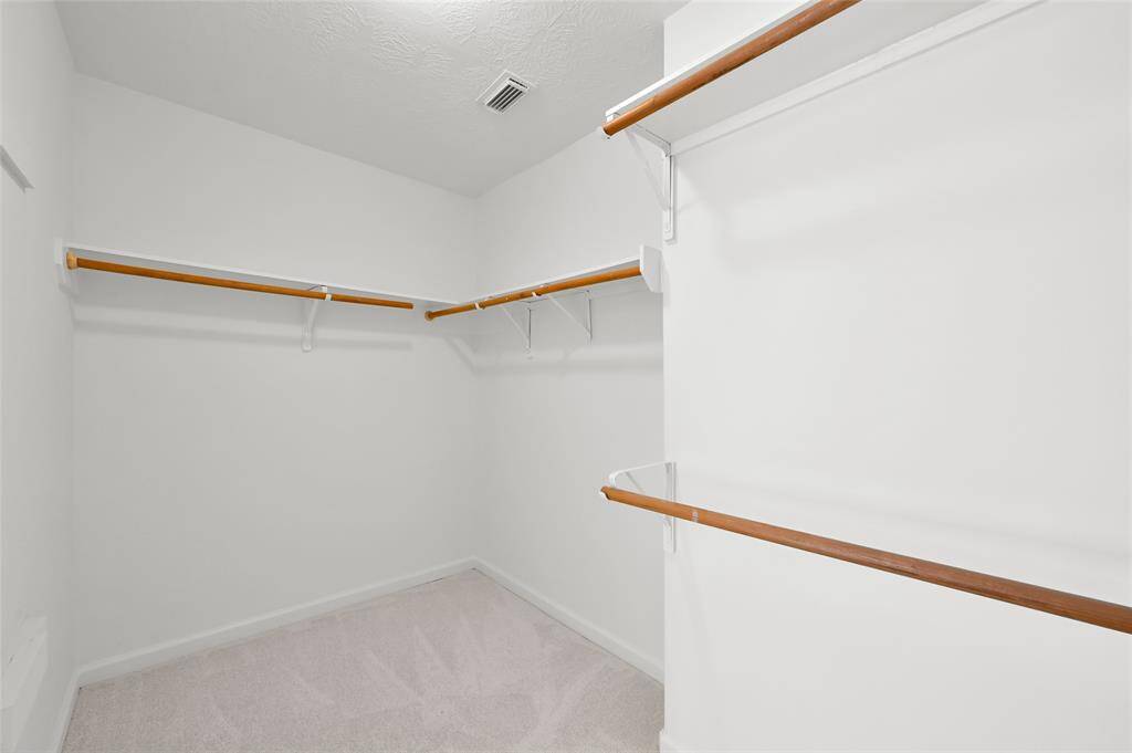This photo shows a spacious walk-in closet with multiple wooden hanging rods and white walls, offering ample storage space for clothing and accessories.