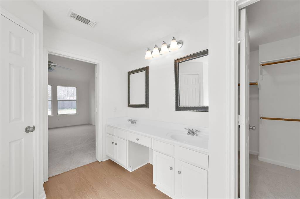 This Primary bath features a double vanity with two mirrors and ample lighting. It connects to a spacious bedroom and a walk-in closet.