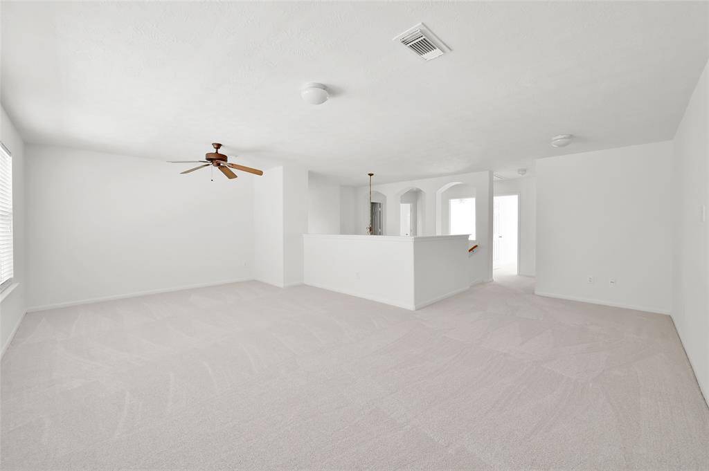This spacious, bright room features fresh white walls and plush carpeting, with ample natural light from large windows. A ceiling fan adds functionality, while doorways lead to adjacent areas, enhancing the open layout. Perfect for versatile living and entertaining.