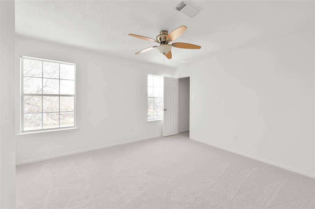 Bright and spacious bedroom with neutral carpeting, large windows for natural light, and a ceiling fan. The room features a door leading to a walk-in closet. Ideal for creating a comfortable retreat.
