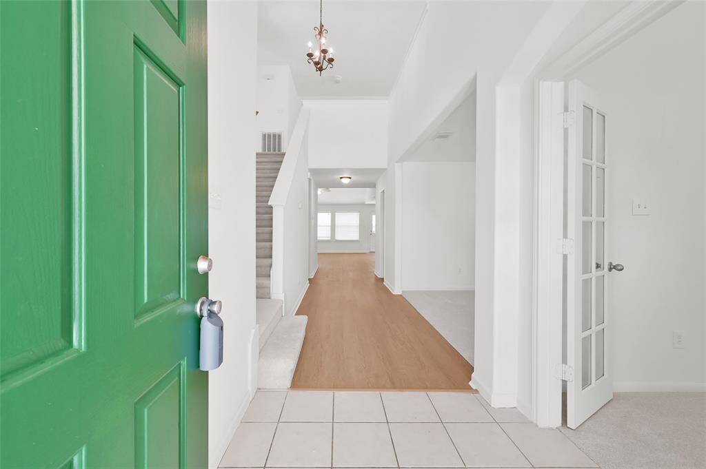 Bright and inviting entryway with a green door, leading to a spacious hallway with wood flooring and carpeted stairs.