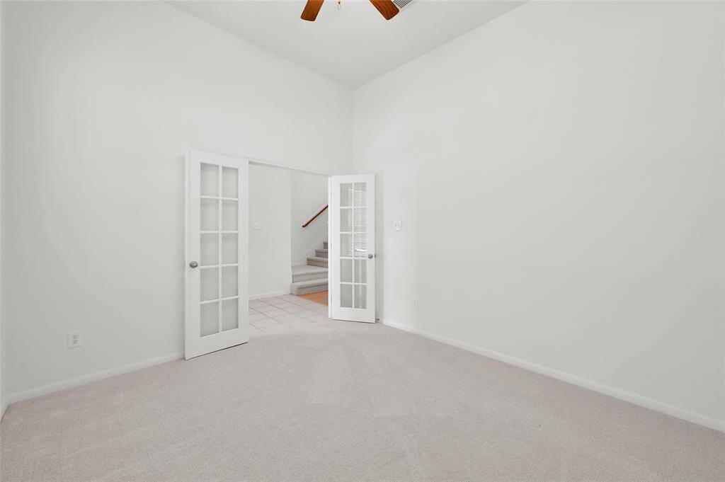 This photo showcases a bright, carpeted room with high ceilings and French doors. Ideal for a flexible living or office space.