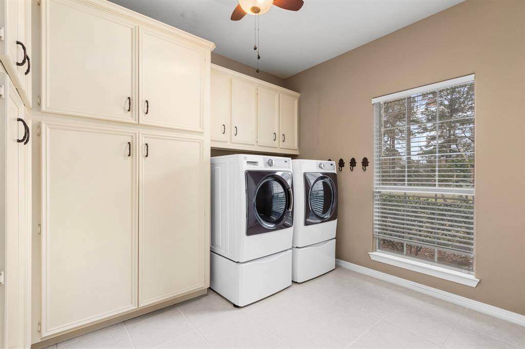 This laundry room features ample cabinetry for storage, a modern washer and dryer set, and a large window providing natural light. The neutral tones create a clean and inviting atmosphere.