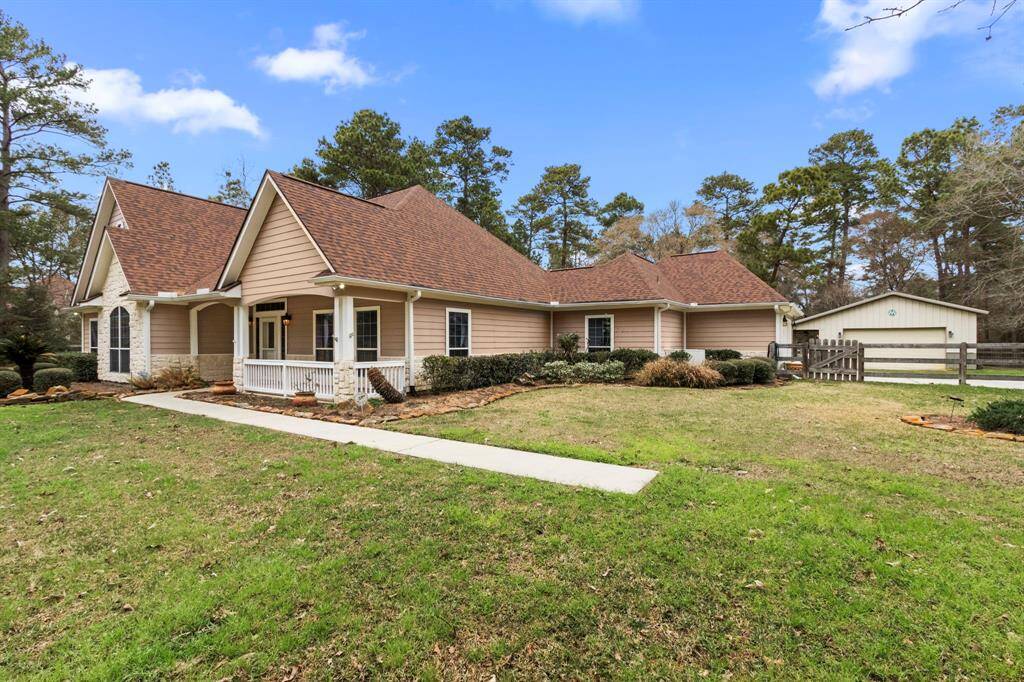 This charming single-story home features a warm, inviting exterior with a gabled roof and a cozy front porch. It's set on a spacious lot with a well-maintained lawn and surrounded by mature trees, offering privacy and a serene atmosphere. A detached garage and fenced yard complete the picture.