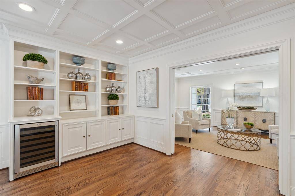 Discover the architecturally appealing built-in bookshelves, custom cabinetry and a stainless beverage refrigerator in the library/den, opposite to the wet bar. The ceiling treatment resembles a box-beam ceiling.