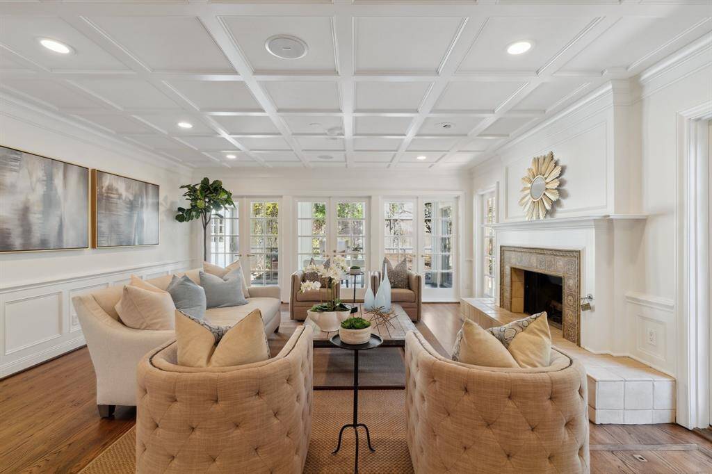 The inviting and ultra-spacious den [26' x 17'] includes wainscoting around the perimeter of the room. The square-paneled ceiling adds visual interest. The fireplace features an elevated Medieval-influenced tile hearth. The sun-filled study beyond is accessible through the pair of French doors flanked by floor-to-ceiling windows.