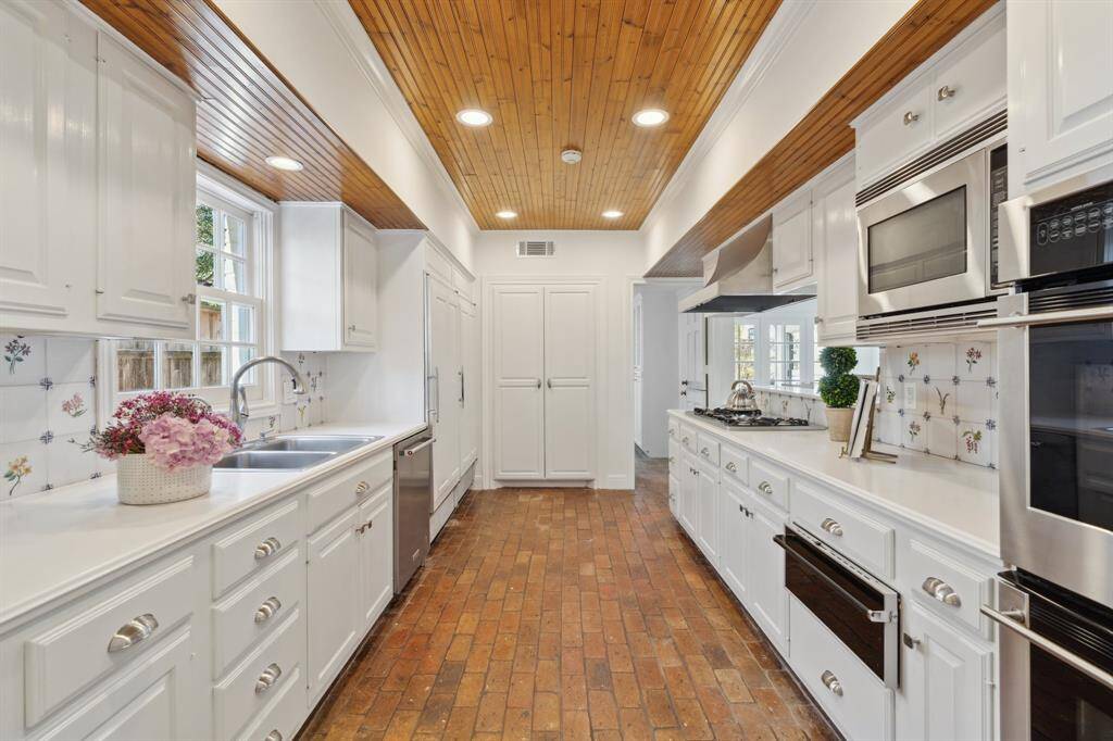 The kitchen's stainless elements include a Thermador cooktop, Vent-a-Hood, dishwasher, double ovens and sink underneath a pretty window. The side-by-side SubZero refrigerator and freezer is to the immediate left of the pantry's double doors. The backsplash offers hand-painted tles, and the white counters are made of Corian. Newly* installed LED recessed ceiling lights and new* satin nickel cabinet hardware. * February 2025 per Seller
