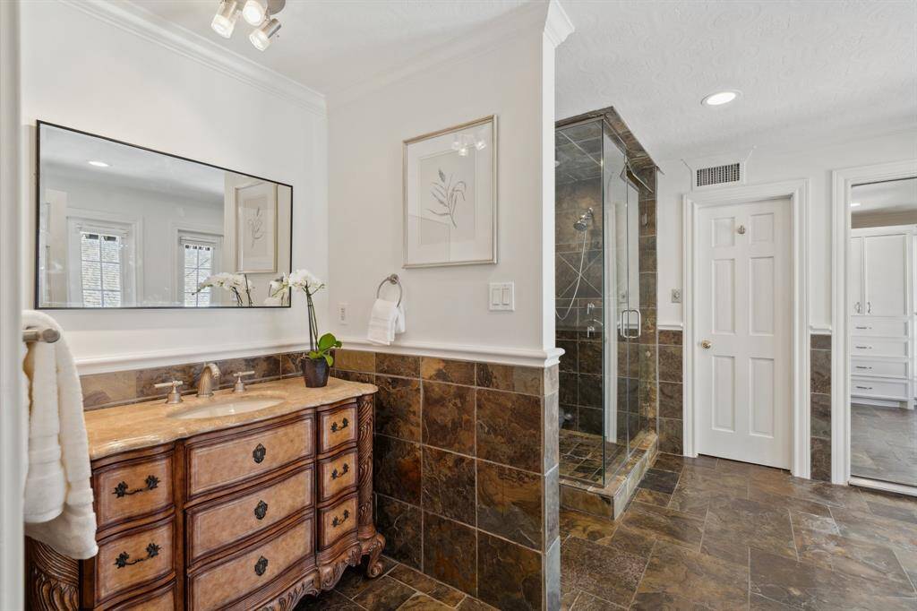 Take a look inside one of two separate primary bathrooms [12' x 12']. The door to the immediate right of the glass-enclosed seamless shower opens to a large walk-in closet complete with a cedar planked ceiling. The floor-to-ceiling doors and windows are visible in the reflection of the vanity mirror. A full length mirror, pictured to the far right, is located in the northwest corner of this full-sized bathroom.
