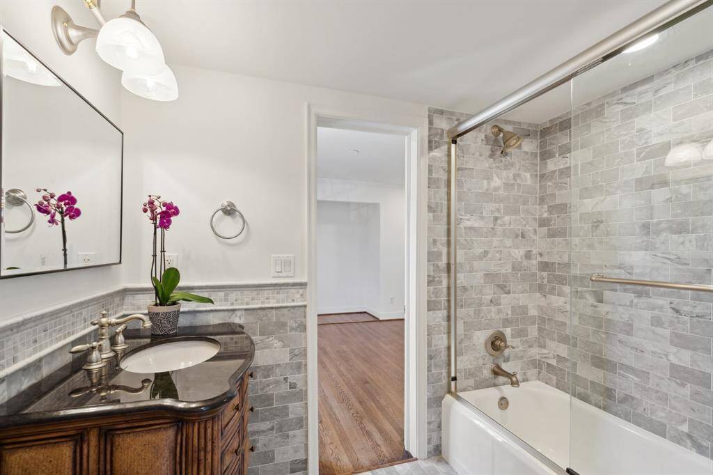 The Hollywood-style marble full bathroom [8' x 6'] is connected to the third and fourth bedrooms Notice how the French-brick style tile wraps around the sink vanity in a horizontal direction and has an added backsplash border behind the faucet. The fourth bedroom is pictured in the background. New mirror-February 2025 per Seller.