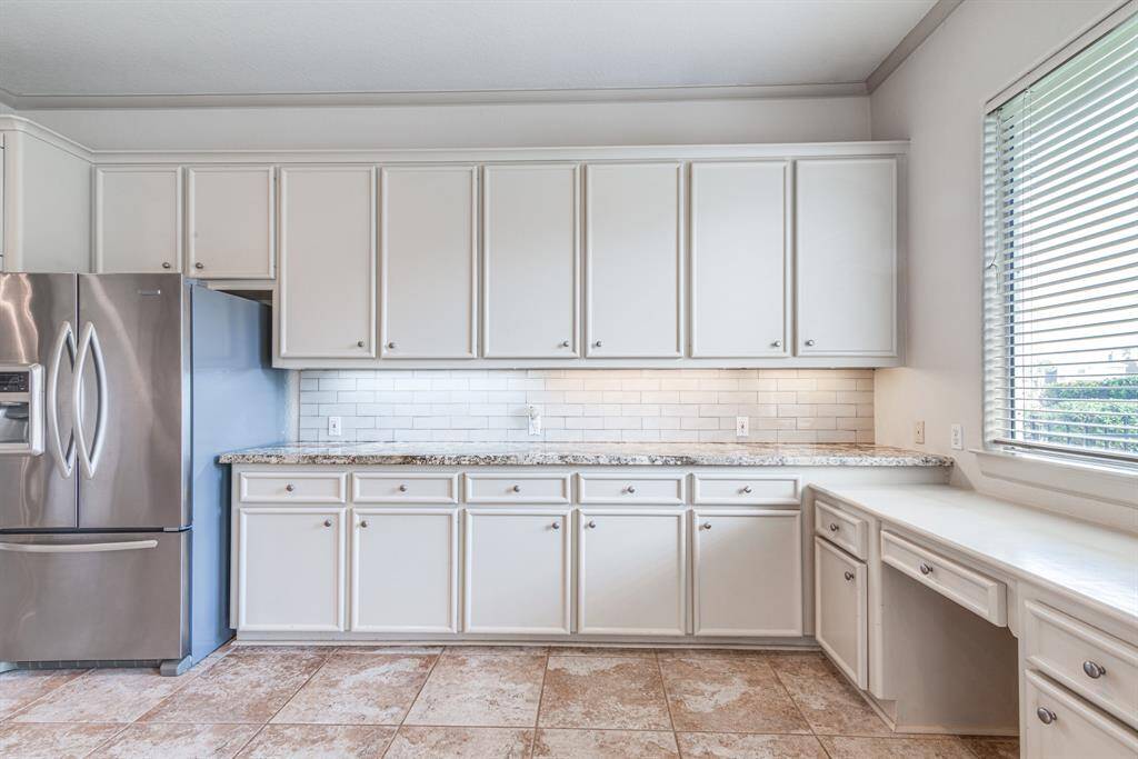 View of the back yard from this convenient desk space. Check out the abundance of cabinetry, beautiful tile back splash and granite counter top.