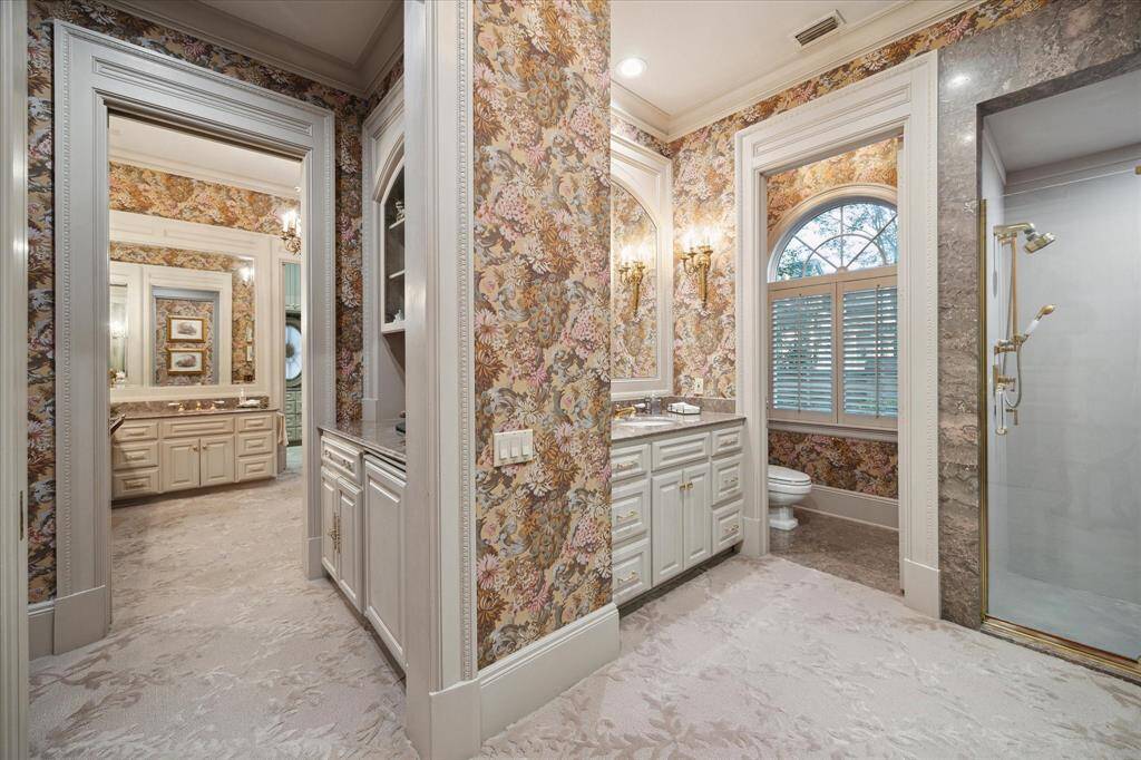 Second primary closet with carpeted flooring, florescent lighting, oculus window, custom millwork, built-in  drawers and shelving, marble countertops, brass hardware, abundant hanging space, and valet rods.