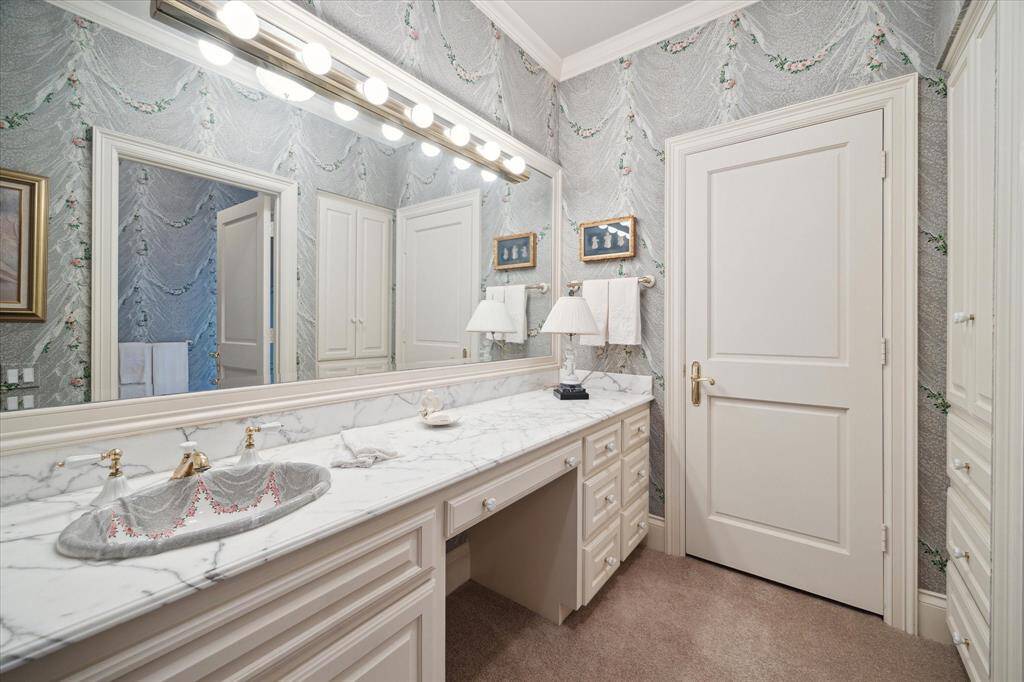 Secondary bedroom with carpeted flooring, custom millwork, plantation shutters, custom drapery, walk-in closest with built-in drawers, shelving, and hanging space, brass knobs and florescent lighting, and is en suite.