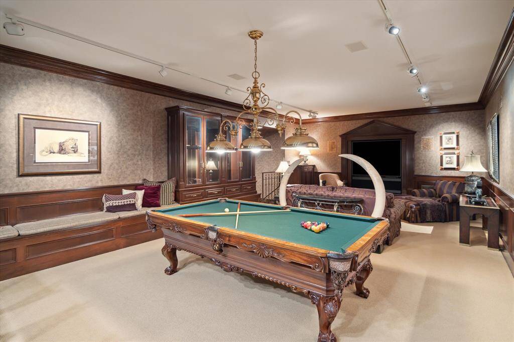 The game room with a wood-paneled wet bar with bar seating, granite countertops, antique brass sink and plumbing fixtures, brass hardware, and built-in ice maker and refrigerator.