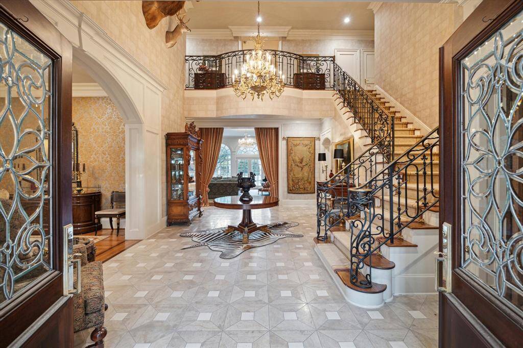 Grand entrance hall with iron entry gates, Mahogany double doors with beveled glass panels, Palladian windows and polished brass hardware, limestone and Lueders tile flooring in a distinctive pattern, ornate brass chandelier, recessed lighting, extensive custom millwork, faux-finished walls, and dual coat closets.