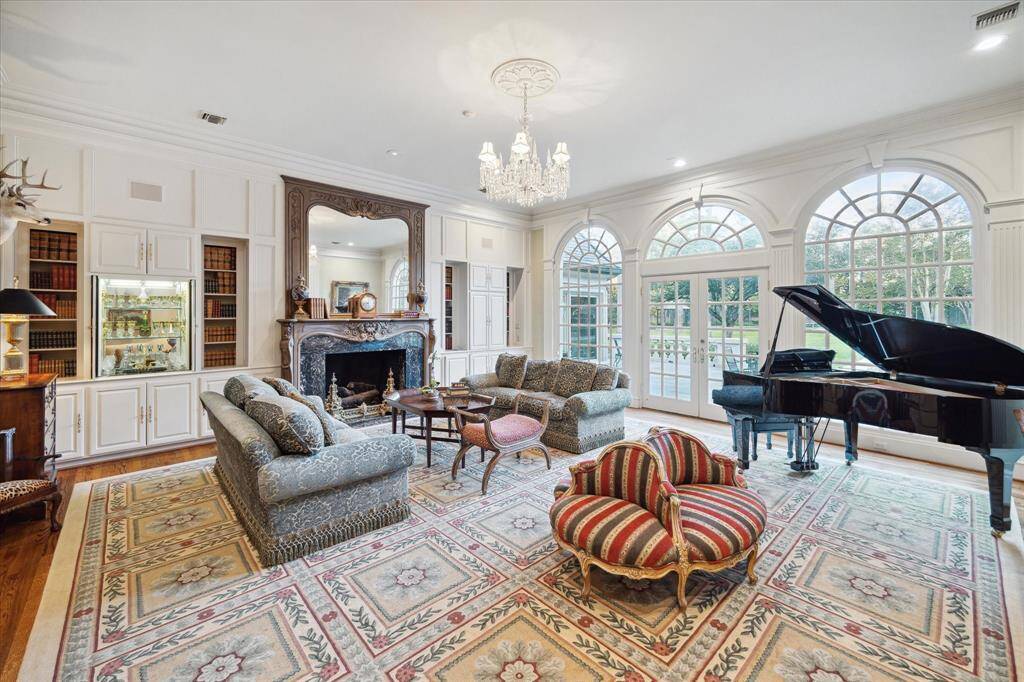Formal living room with oak hardwood floors, high ceilings, crystal chandelier with a ceiling medallion, recessed lighting, custom millwork, wood burning fireplace with a faux finished mantle, marble surround and gas logs, built-in cabinetry and shelving, brass hardware, French doors to the garden, palladian windows, built-in wet bar with a marble countertop, ceramic sink, and brass and crystal plumbing fixtures, and built-in speakers.
