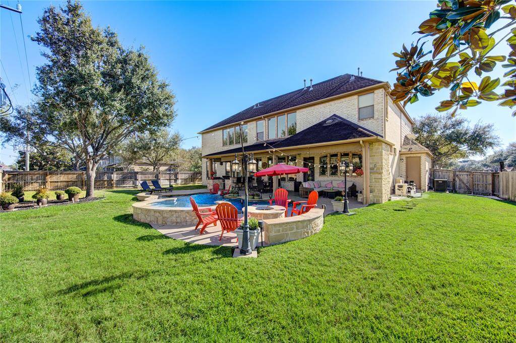 This photo showcases a spacious backyard featuring a well-maintained lawn, outdoor living space perfect for entertaining, resort style pool, and mature trees providing shade