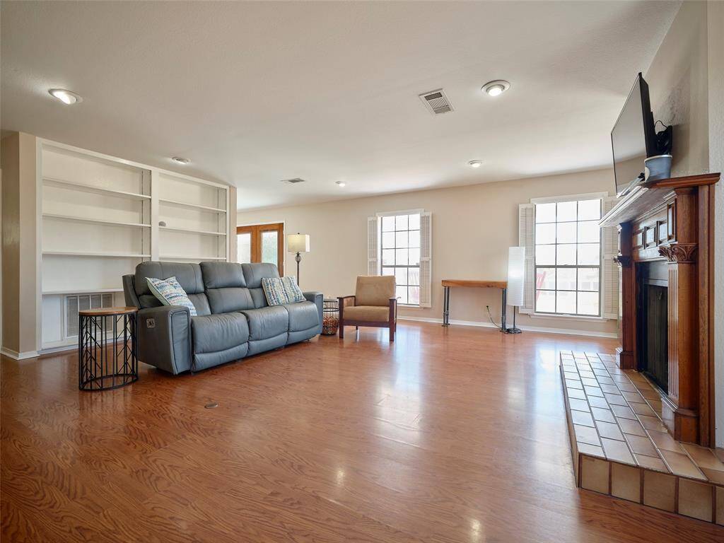 Spacious living room with hardwood floors, a classic fireplace, built-in shelving, and ample natural light from large windows.