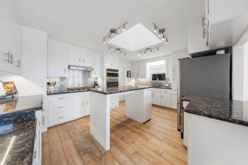 The sleek and modern kitchen features granite countertops, crisp white cabinets with stylish hardware, and contemporary light fixtures, creating a perfect blend of elegance and functionality.