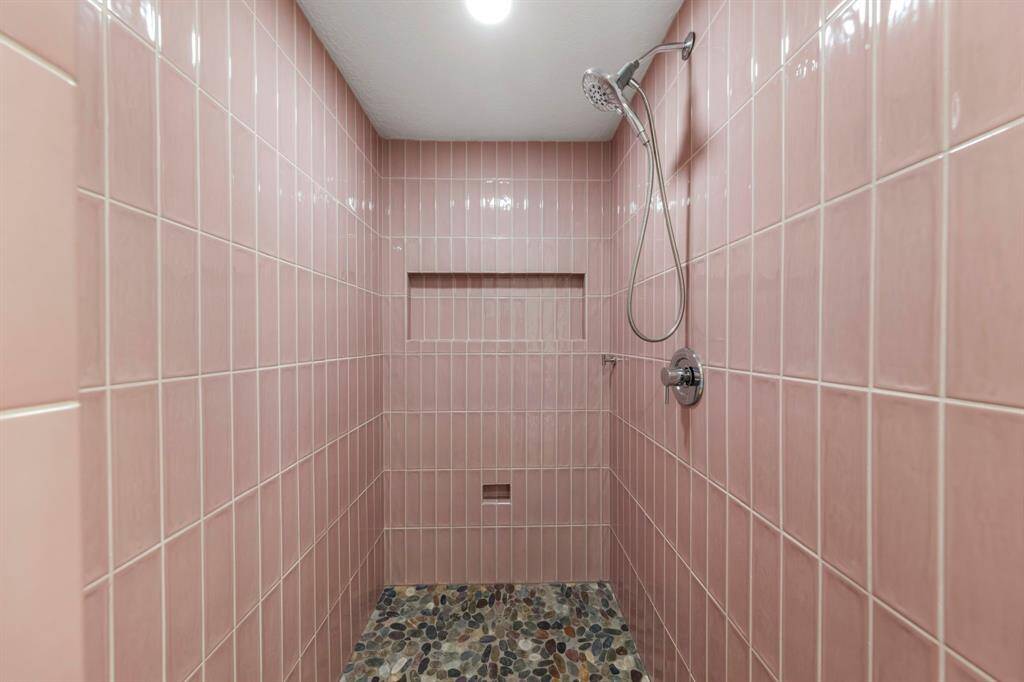 A chic floor-to-ceiling tiled shower features a built-in nook for products and a sleek stone floor, adding both style and functionality.